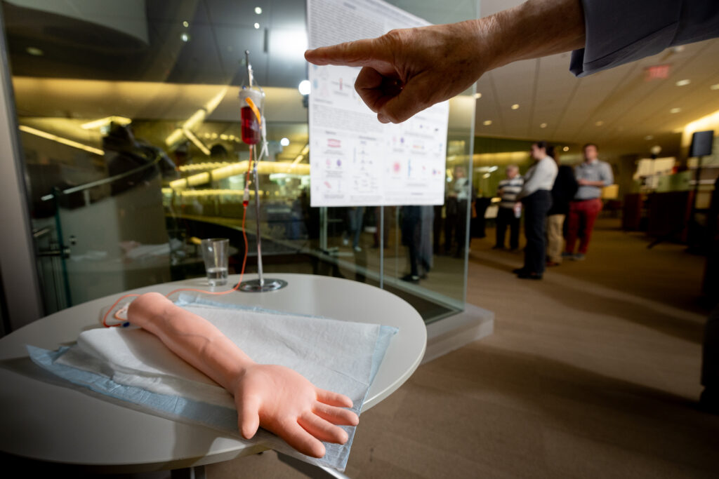 Lab members use a model arm to explain the blood draw procedures used to collect samples.