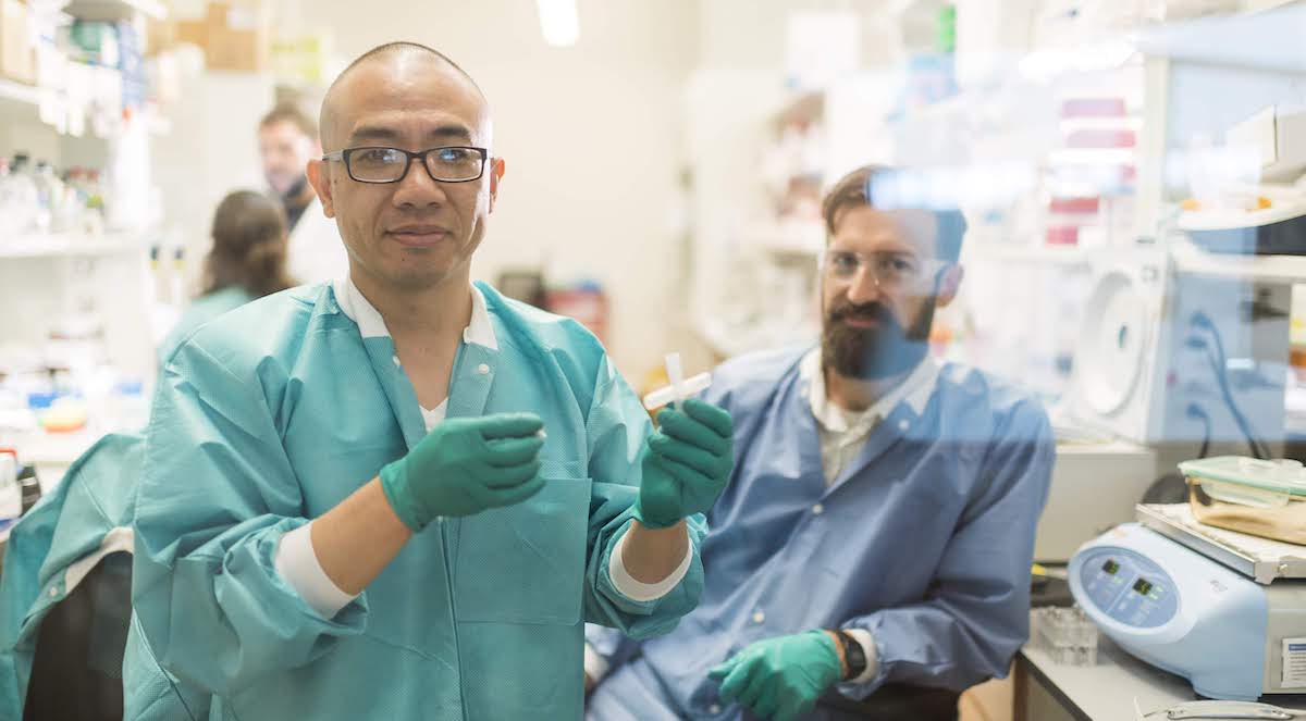 Two scientists in blue lab coats pose in the laboratory.