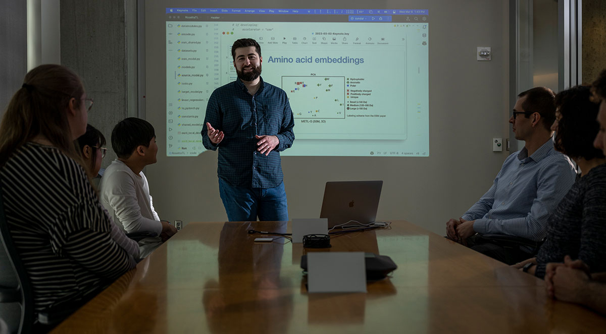 Sam Gelman speaking in front of colleagues in a conference room.